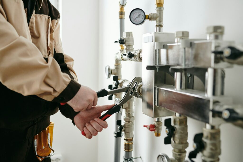 Man in plumber uniform using a tool while repairing pipe